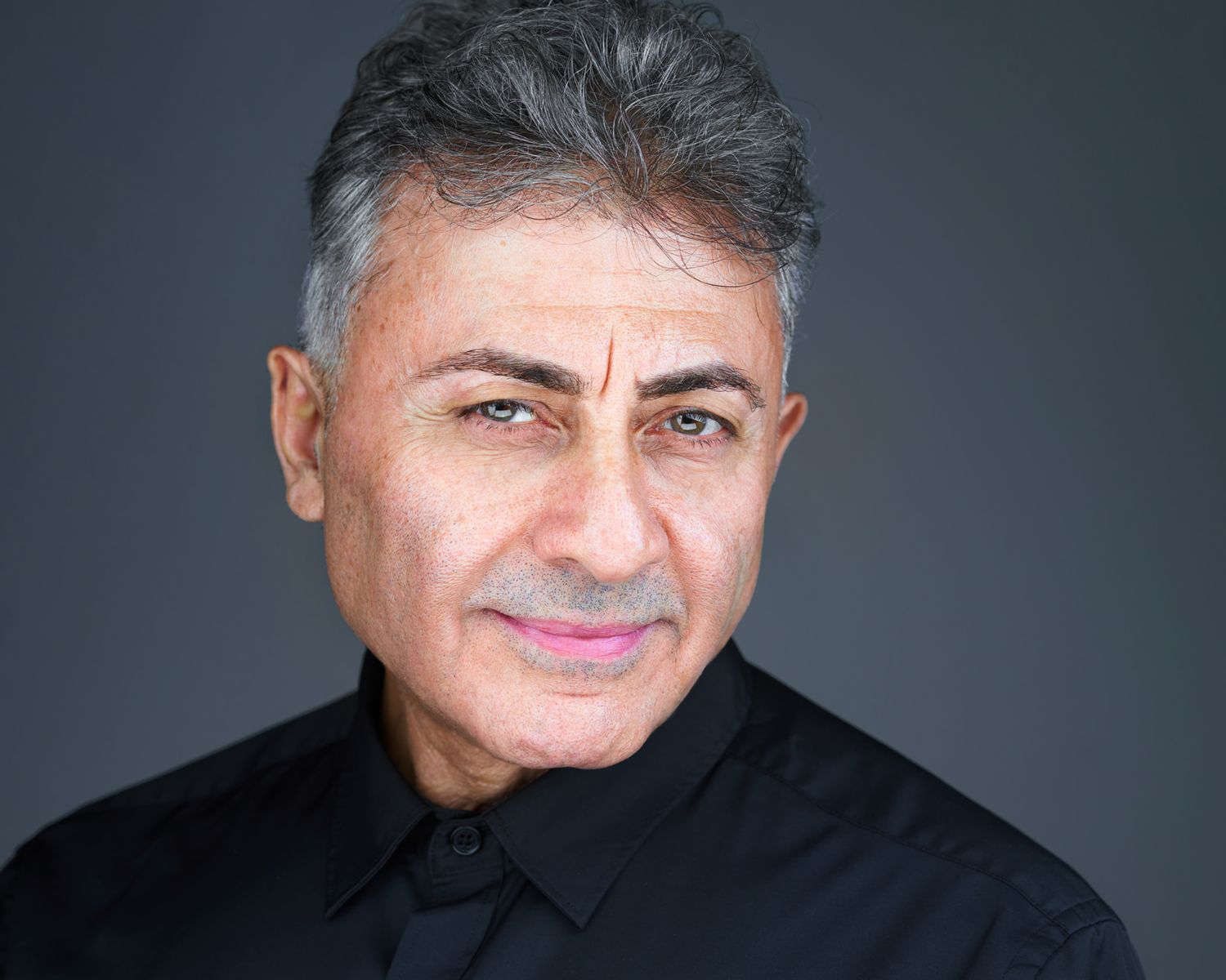 Business Headshot of a man with a black shirt and no tie on a dark background taken by Kalin Tabov Photography in Irvine, CA.