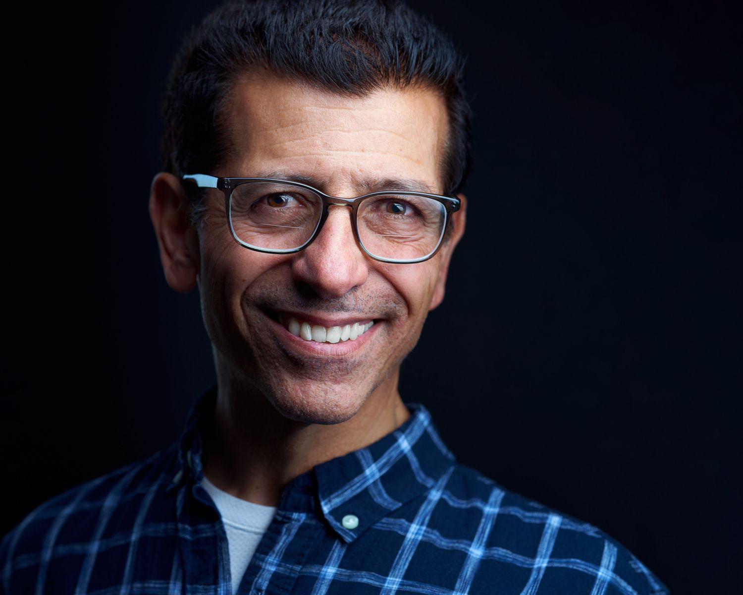 Business Headshot of a man with glasses and a blue shirt on squares on a dark background taken by Kalin Tabov Photography in Irvine, CA.