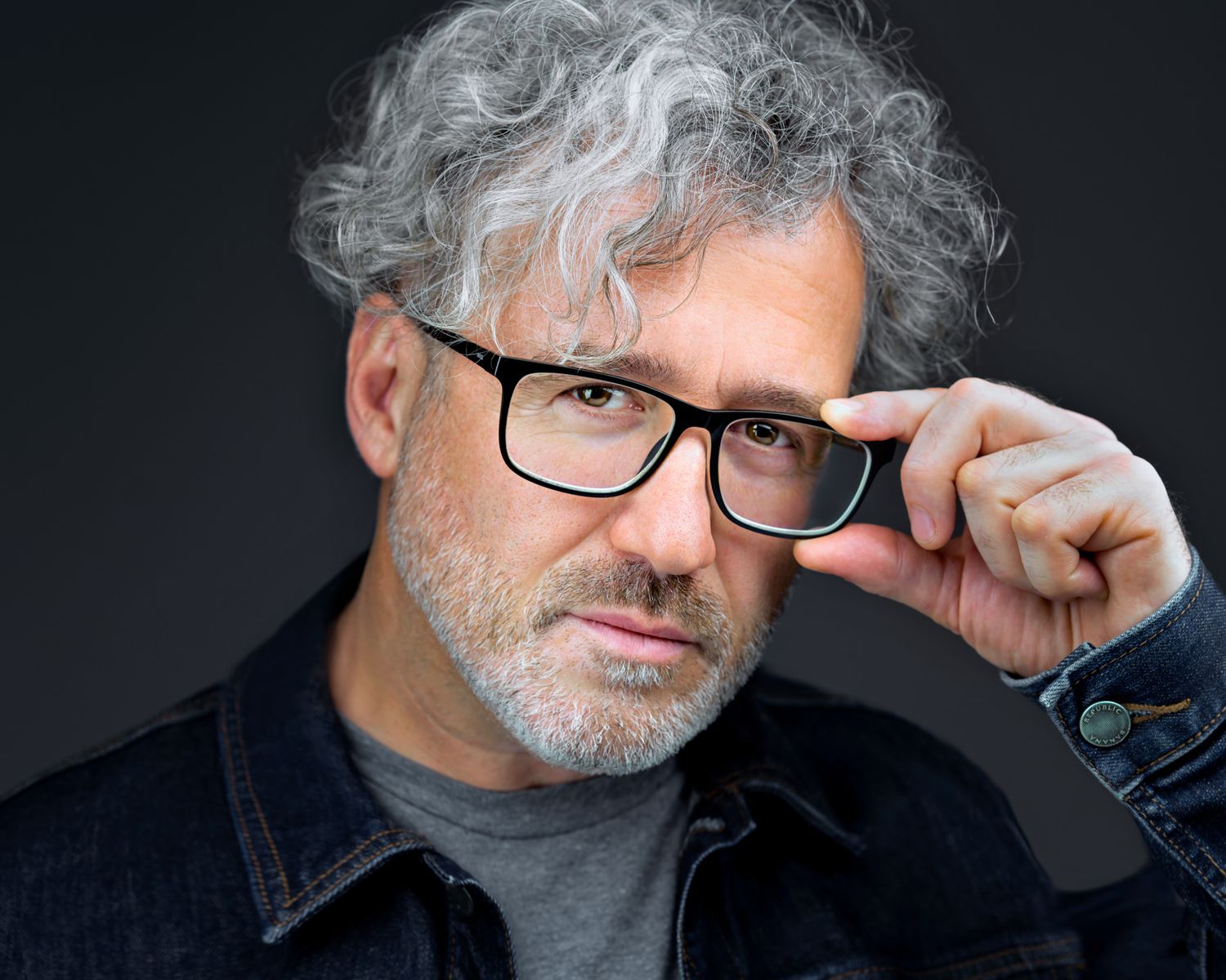 Business Headshot of a man with glasses, dark jean jacket and blue shirt on a dark background taken by Kalin Tabov Photography in Irvine, CA.