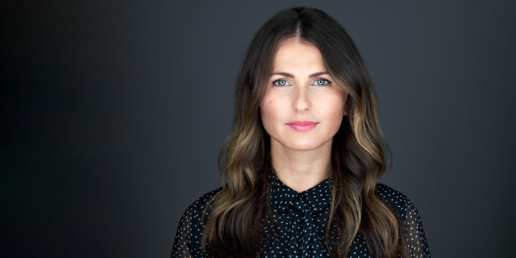 High end headshot of a white woman with brown hair on a dark gray background